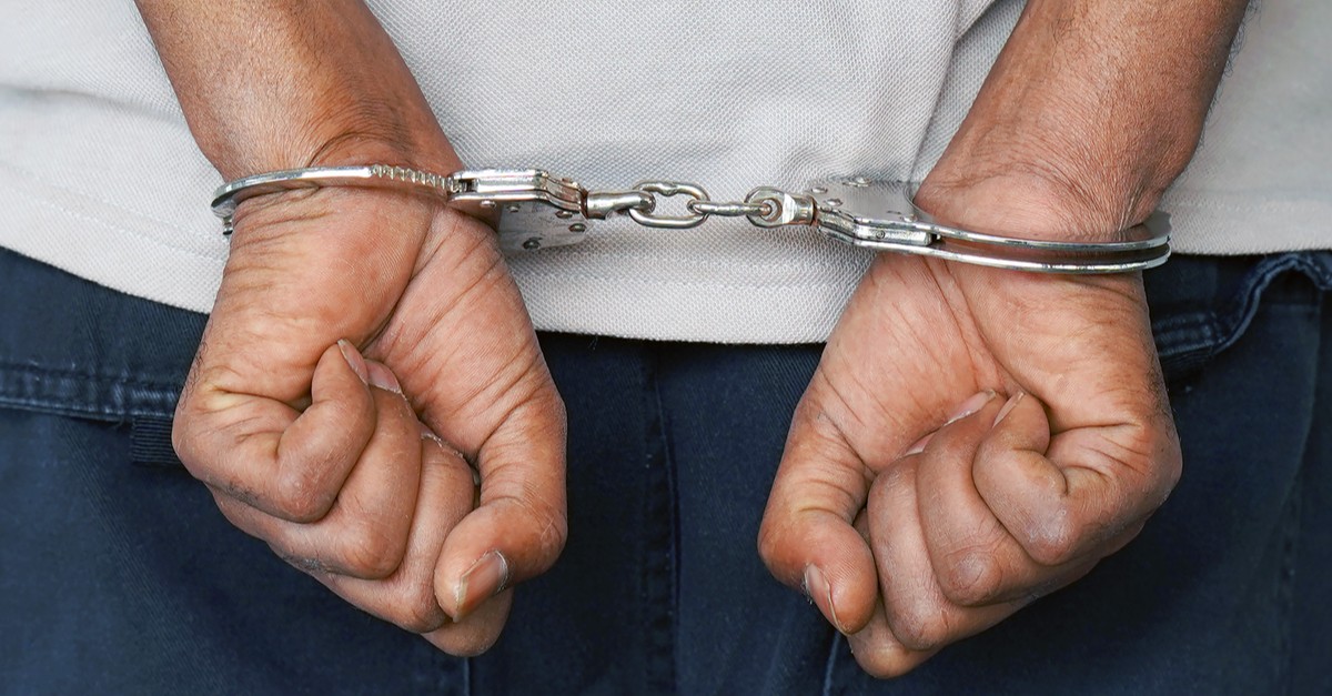 man handcuffed hands at the back isolated on gray background-img