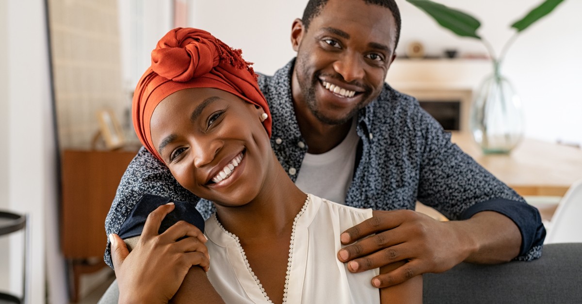 Portrait of mid adult happy african american couple hugging at home while sitting on couch-img