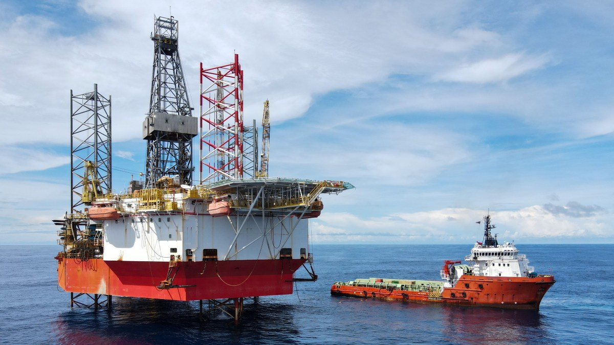 A jack up rig with an anchor handling vessel during cargo operation at sea-img