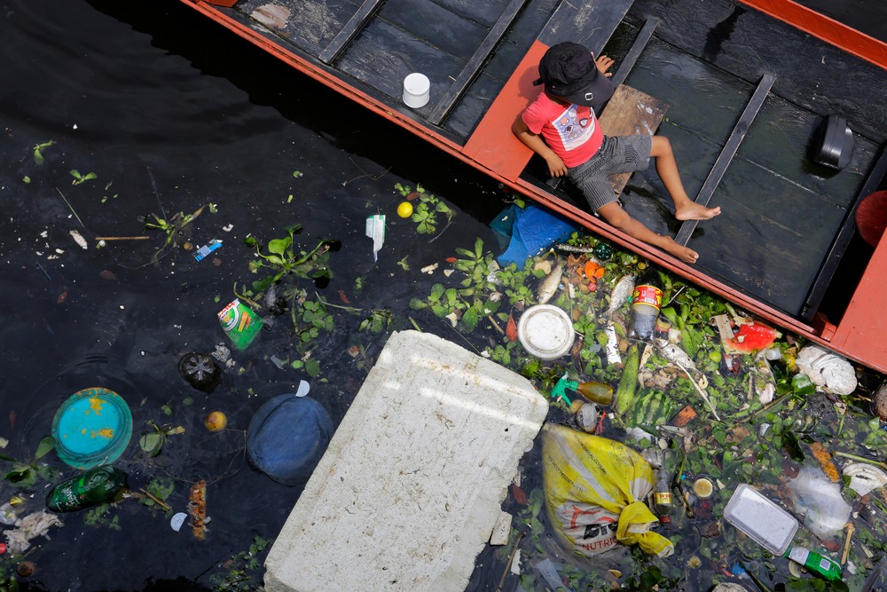 A child is seen in a boat next to a pile of trash inside an urban region of Negro River-img