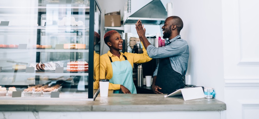 Cheerful black man and woman in aprons giving high five to each other-img