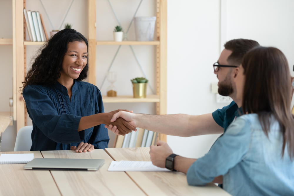 Real,Estate,Agent,Shaking,Hands,With,Happy,Young,Couple,In
